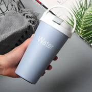 Light blue matte-finish insulated travel mug with a white lid and handle, featuring the word ’water’ printed in subtle white lettering.
