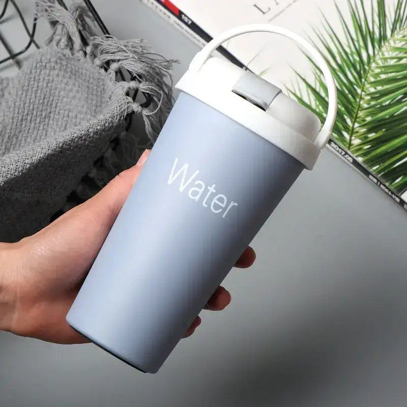 Light blue matte-finish insulated travel mug with a white lid and handle, featuring the word ’water’ printed in subtle white lettering.