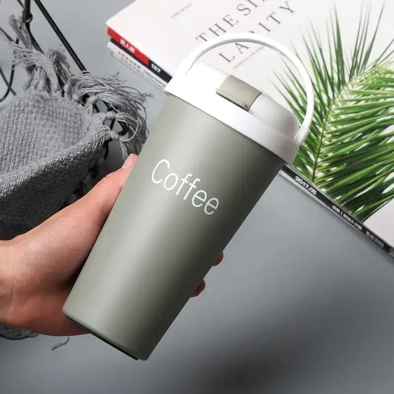 A matte olive green insulated travel mug with a white lid and handle, featuring the word ’coffee’ printed in elegant white script.
