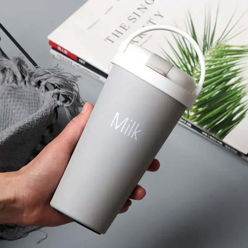 Gray insulated travel mug with white lid and handle, featuring the word ’milk’ in subtle silver lettering.