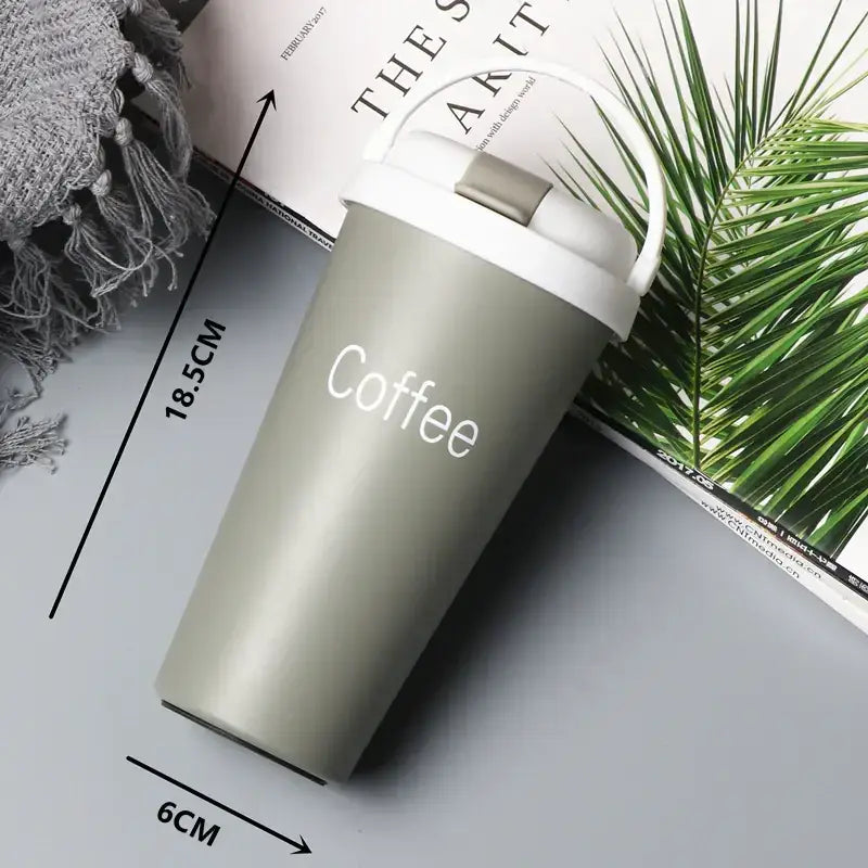 A sleek matte sage green insulated travel mug with a white lid and handle, featuring the word ’coffee’ printed in clean white lettering.