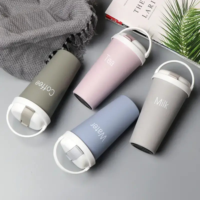 Three pastel-colored insulated travel mugs with white lids and handles, each labeled ’coffee,’ ’tea,’ or ’milk’ in a minimalist font.