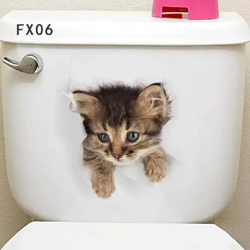 A brown and black tabby kitten with blue eyes peeks through a hole in the white toilet tank, its fur appearing soft and fluffy.