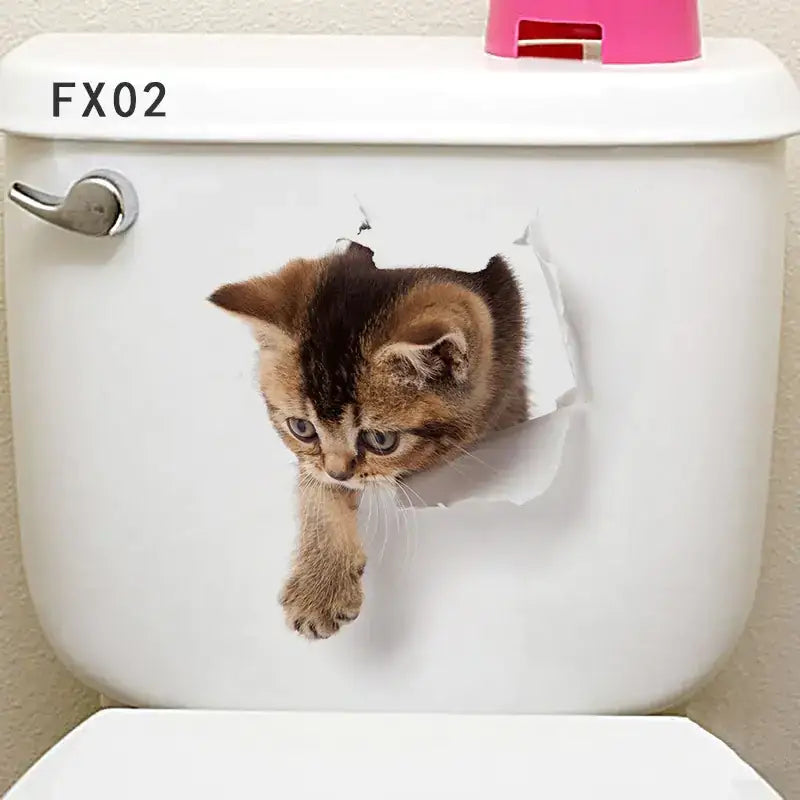 Adorable brown and black kitten peeking through a torn paper effect decal on a white toilet tank.