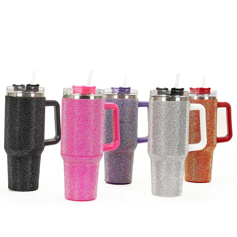 Five sparkling, rhinestone-encrusted insulated tumblers in black, pink, purple, silver, and orange with matching colored handles and lids.