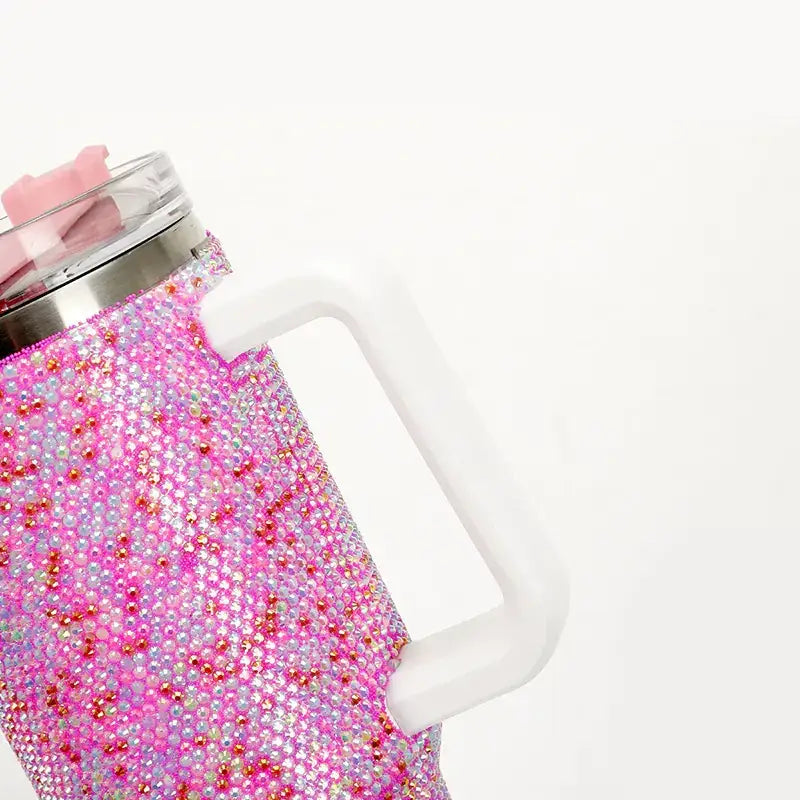 A pink rhinestone-encrusted insulated mug with a white handle and clear lid featuring a pink silicone bear-shaped sipper.