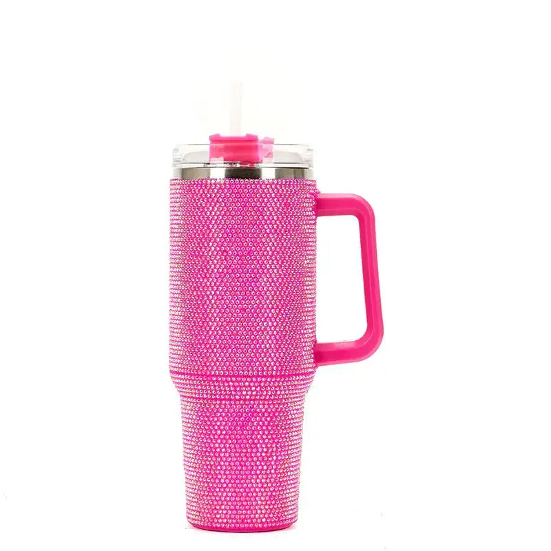 A vibrant pink insulated tumbler adorned with a dense layer of sparkling rhinestones, featuring a matching handle and a clear lid with a straw.