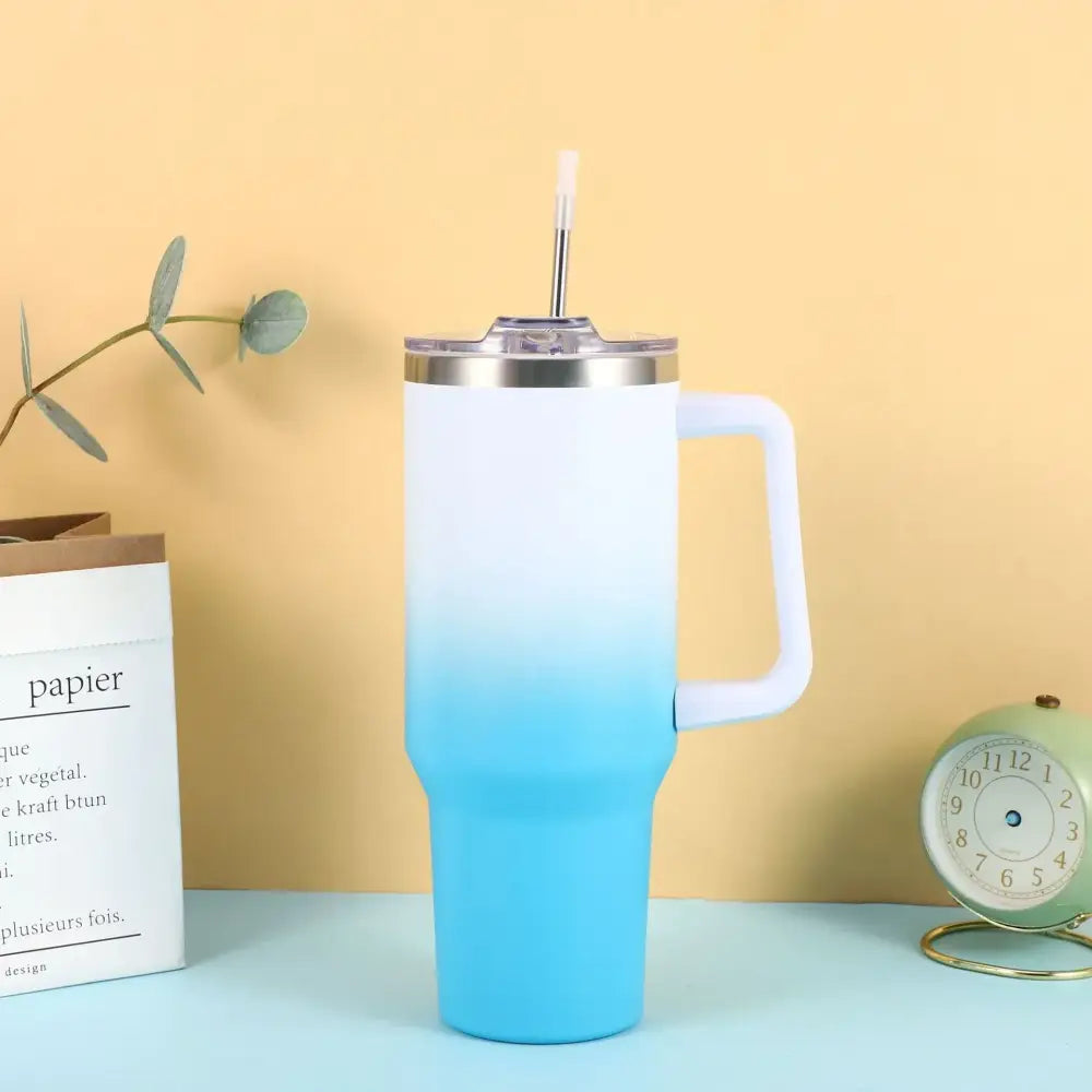 A sleek white-to-blue gradient insulated tumbler with a stainless steel lid and handle, featuring a clear straw.