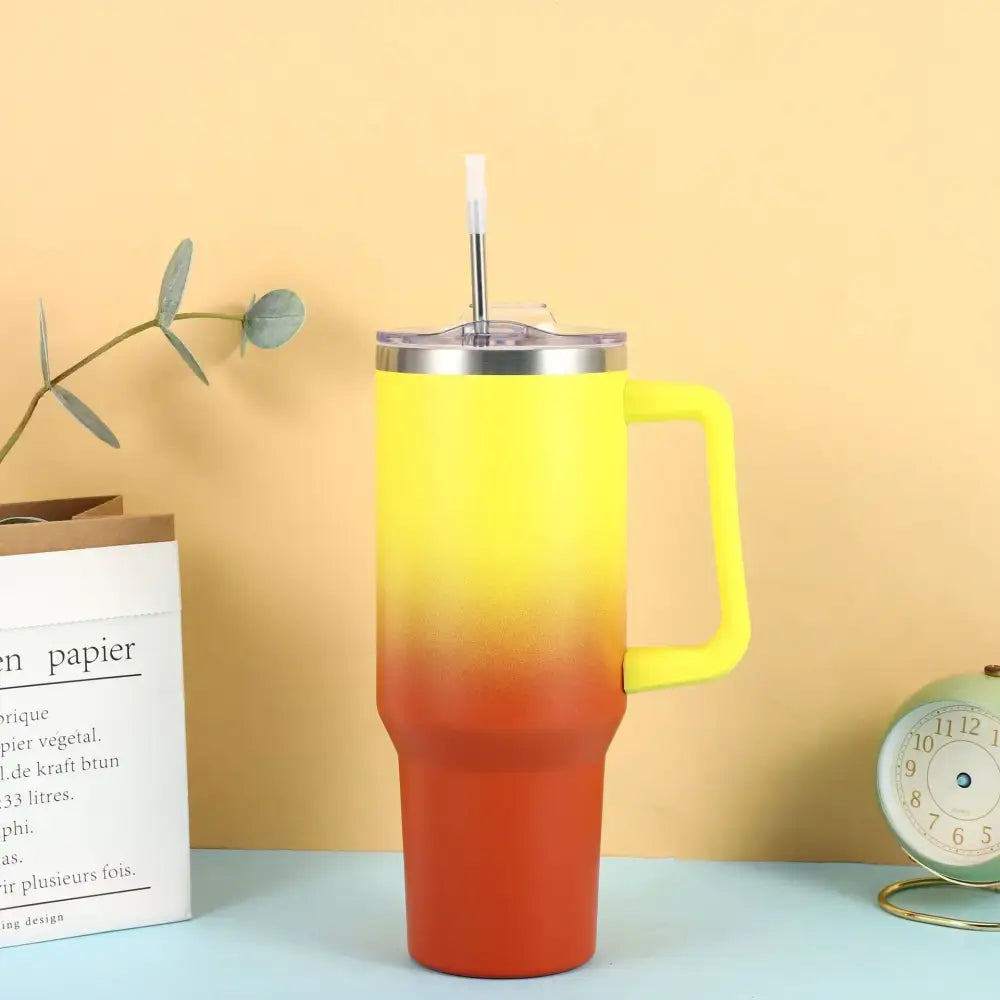 A vibrant yellow-to-orange gradient insulated tumbler with a matching handle and clear lid, featuring a stainless steel straw.