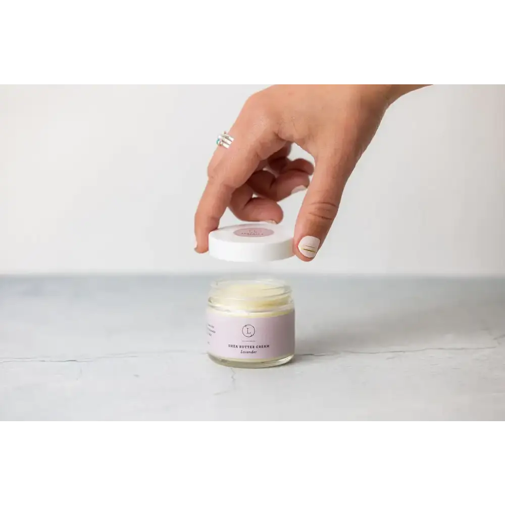 A lavender-scented shea butter cream in a clear glass jar with a white lid and minimalist purple label.