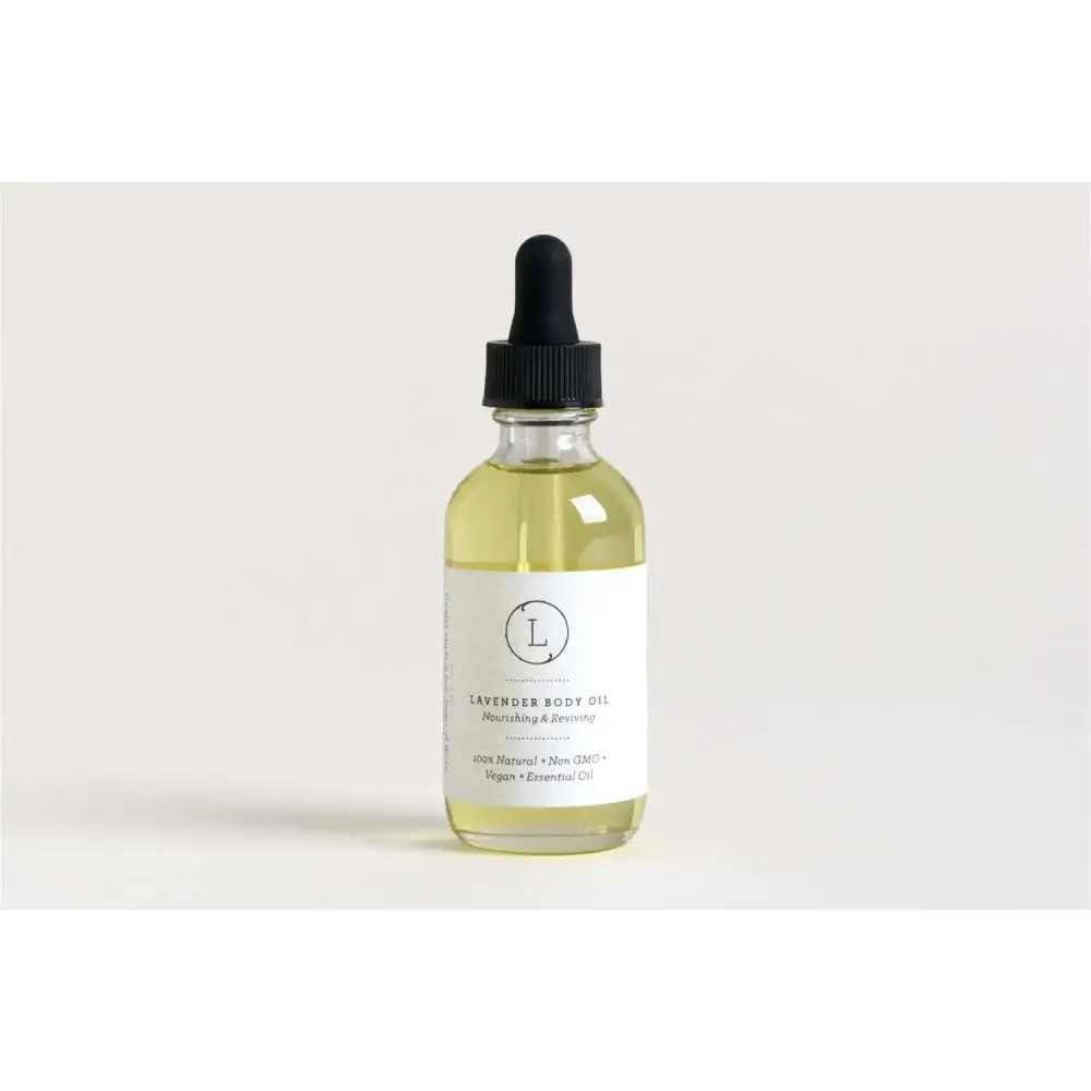A clear glass bottle with a black dropper cap contains pale yellow lavender body oil, labeled ’lavender body oil’ on a minimalist white label.