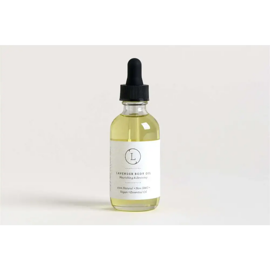 A clear glass bottle with a black dropper cap contains pale yellow lavender body oil, labeled ’lavender body oil’ on a minimalist white label.