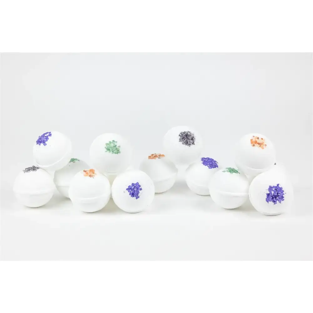 White spherical bath bombs with colorful, glittery floral toppings in shades of purple, green, and orange.