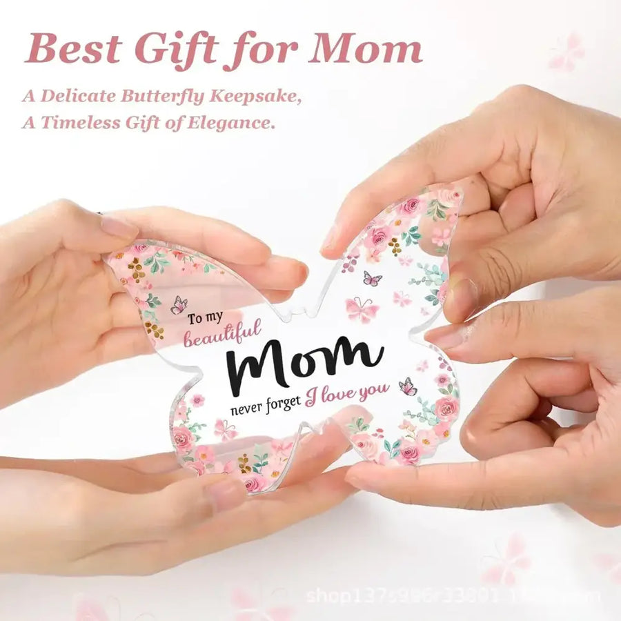 A clear, butterfly-shaped keepsake with a delicate floral pattern in pink and green hues, featuring the inscription ’to my beautiful mom never forget i love you’ on its center.