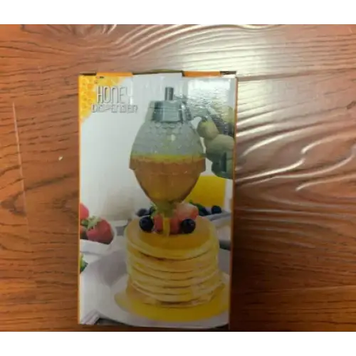 The honey dispenser is a clear glass container with a silver-toned metal top and spout, designed to hold and dispense golden honey.