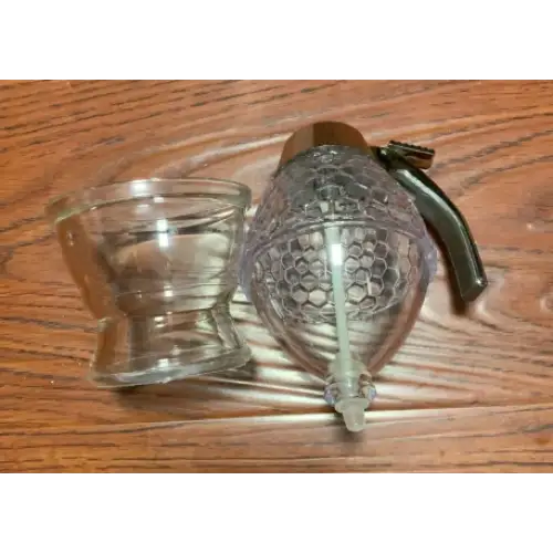 Clear glass honey dispenser with a textured, hexagonal pattern and a dark green handle.