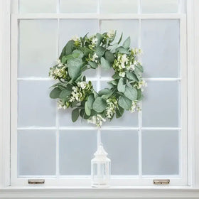 A lush green eucalyptus wreath adorned with delicate white flowers hangs gracefully on a window.