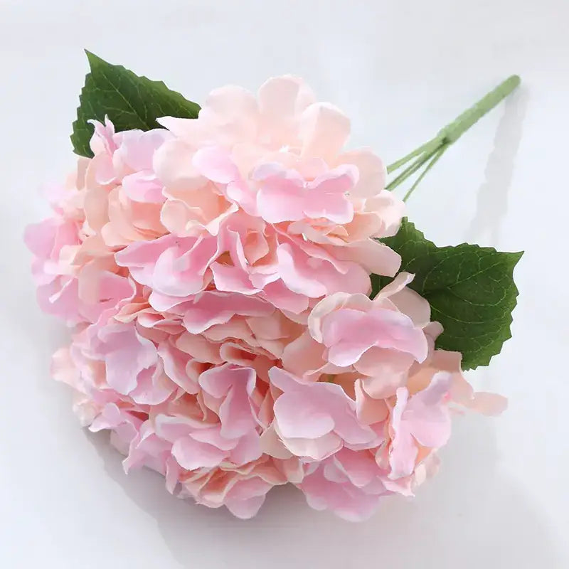A delicate pink hydrangea bouquet with soft, layered petals and vibrant green leaves.