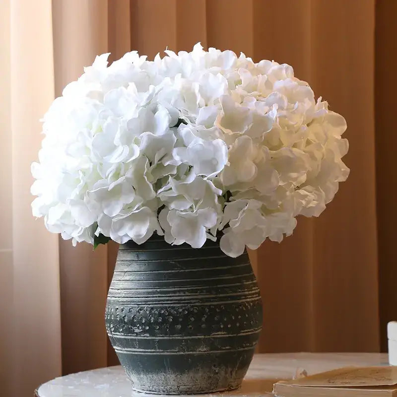 A lush arrangement of white hydrangeas in a rustic, dark green ceramic vase with horizontal ridges and dotted texture.