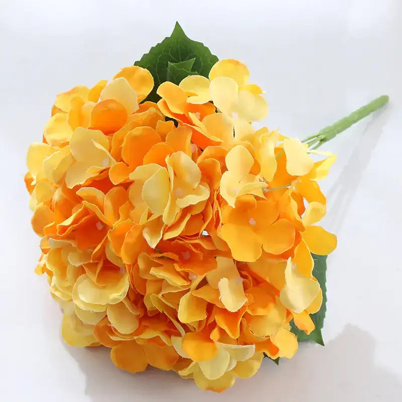A vibrant orange and yellow artificial hydrangea bouquet with lush, layered petals and green leaves.