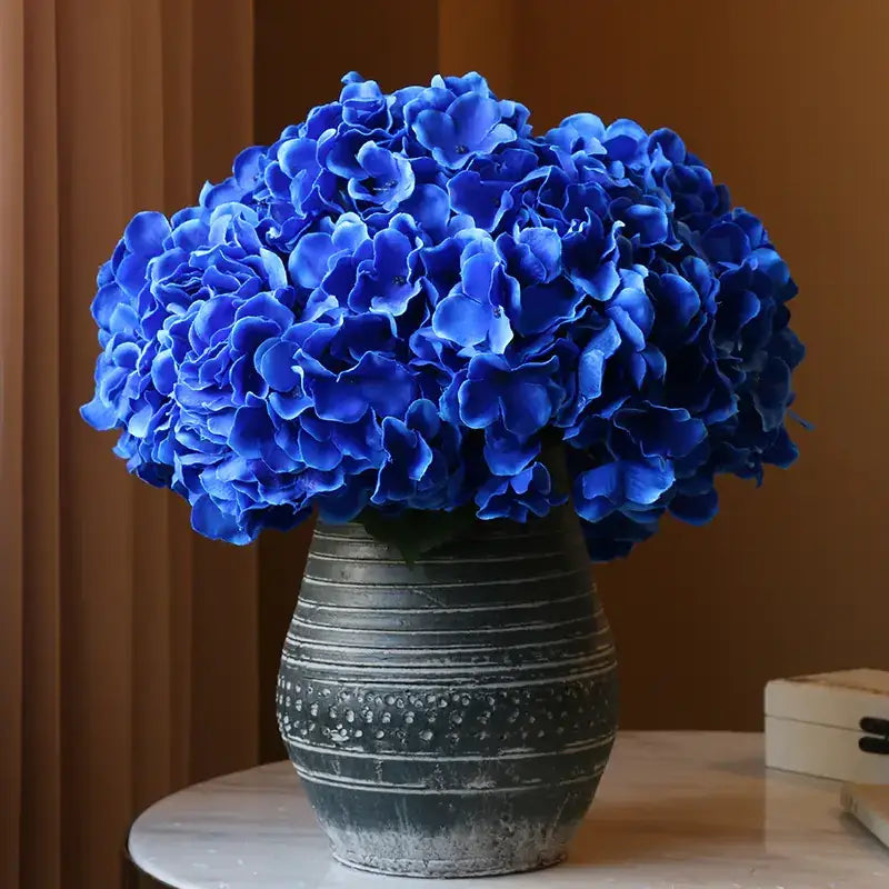 Vibrant royal blue artificial hydrangeas in a distressed gray ceramic vase.