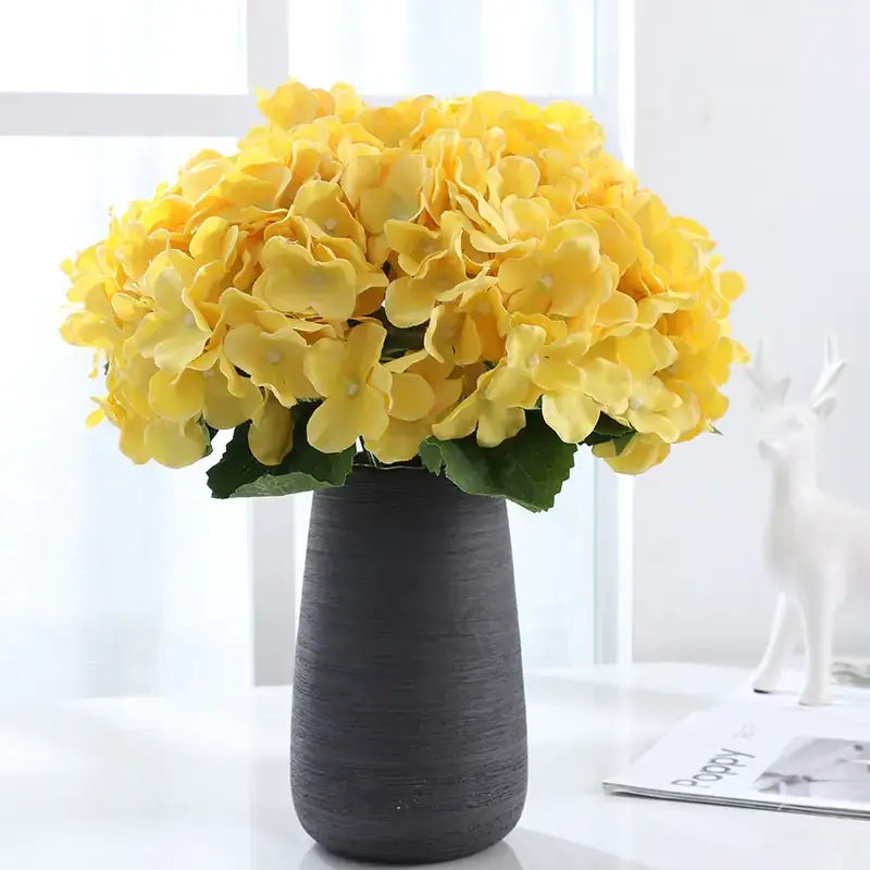 A vibrant yellow artificial hydrangea bouquet arranged in a textured dark gray ceramic vase.