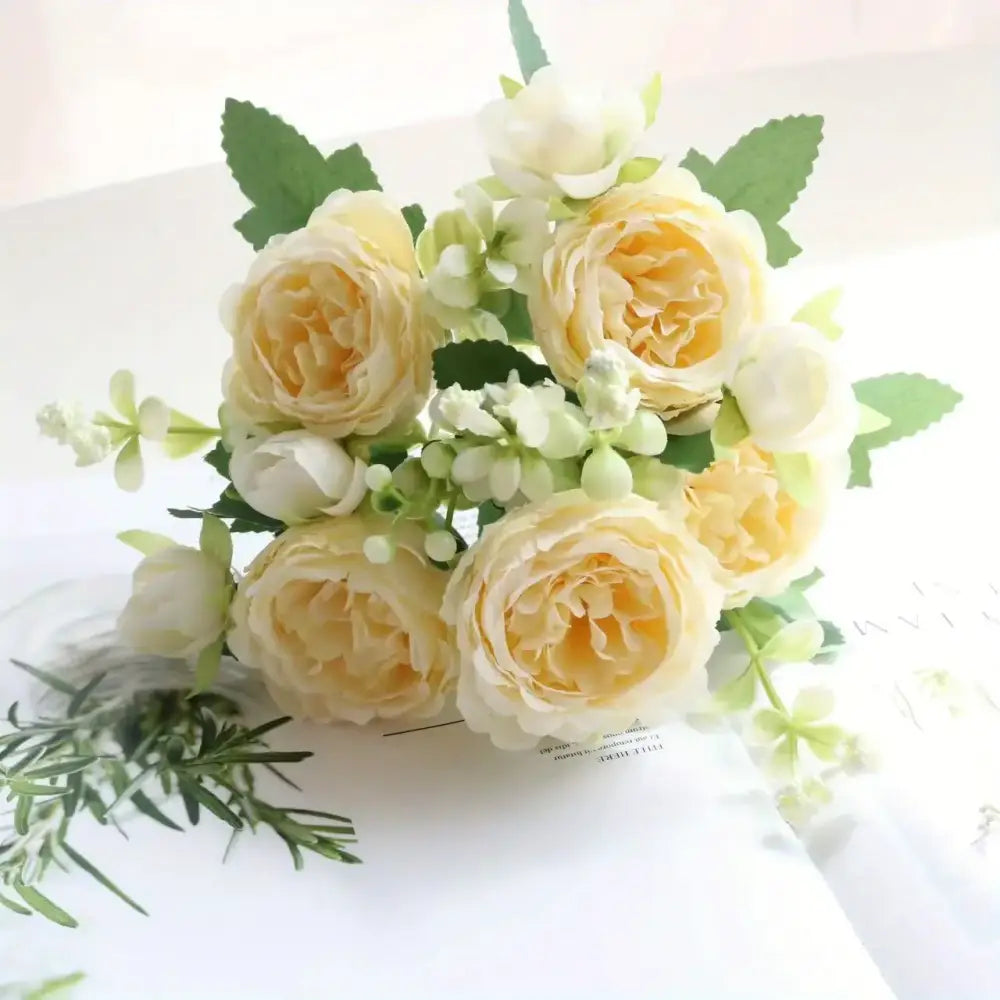 A delicate bouquet of cream and pale yellow artificial roses with green leaves, arranged in a soft, romantic cluster.