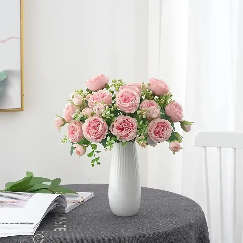 A delicate arrangement of pink roses and greenery in a sleek white ceramic vase.