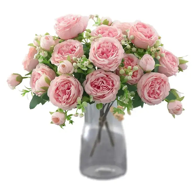A bouquet of delicate pink roses with green leaves and small white blossoms arranged in a clear glass vase.