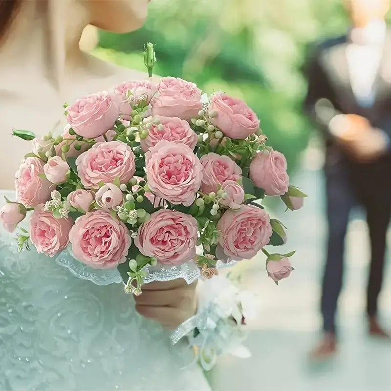A delicate bouquet of soft pink roses, accented with tiny white blossoms and greenery, elegantly wrapped in a lace ribbon.
