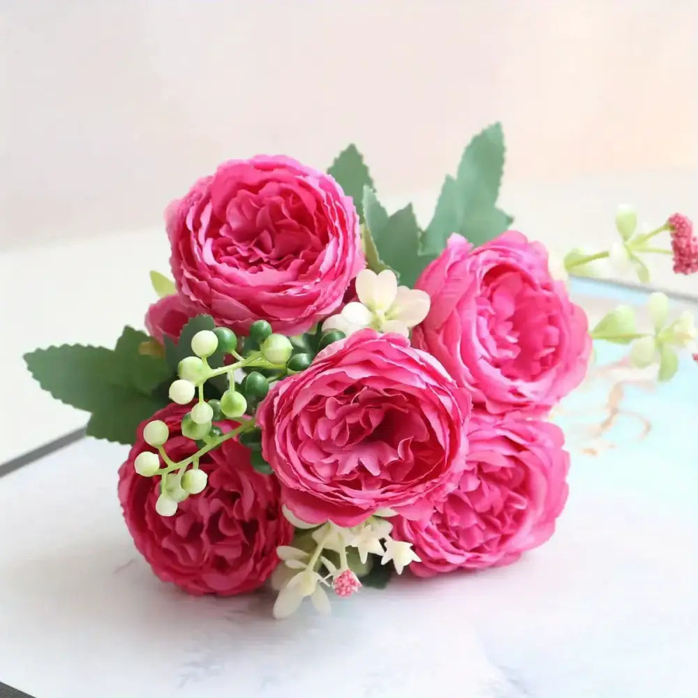 A vibrant pink artificial rose bouquet with lush, layered petals and accented by small white flowers and green berries.