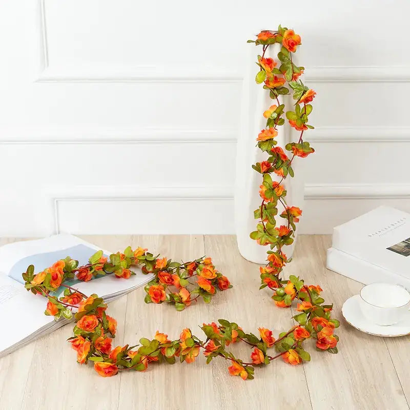 A vibrant orange and green artificial flower garland with realistic petals and leaves, arranged in a flowing vine pattern.