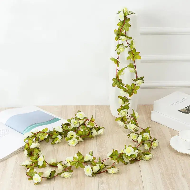 A delicate white and green artificial floral garland with realistic-looking blossoms and leaves, strung along a slender vine.