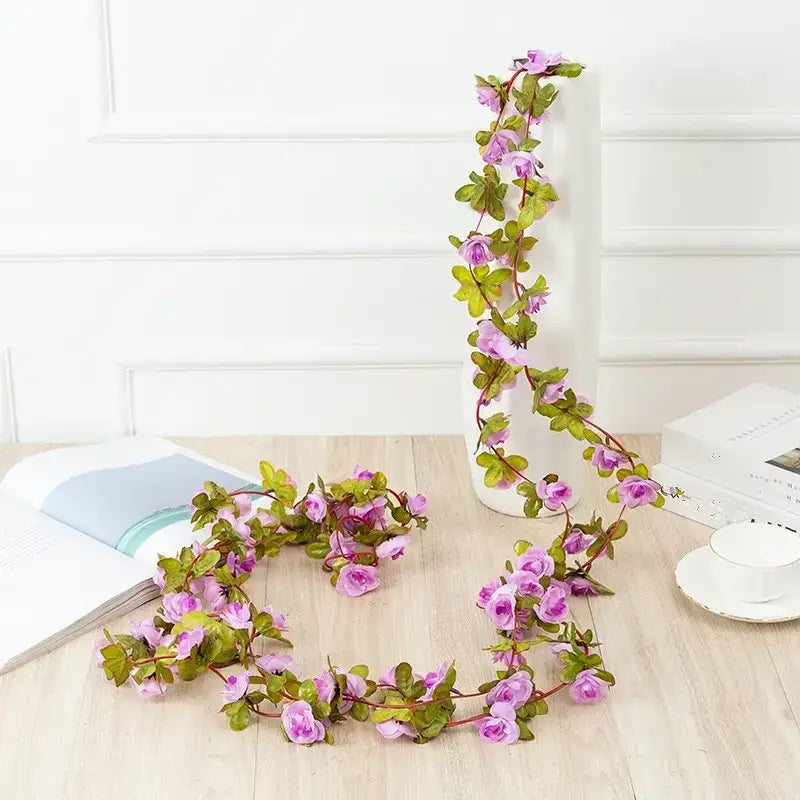 A delicate artificial floral garland with soft pink blossoms and green leaves, crafted from synthetic material to mimic the look of real vines.
