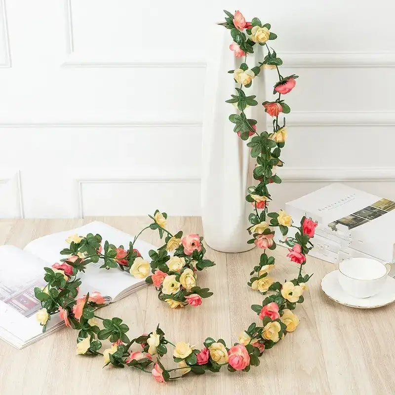 A delicate floral garland featuring artificial roses in soft pink and yellow hues, accented with lush green leaves.