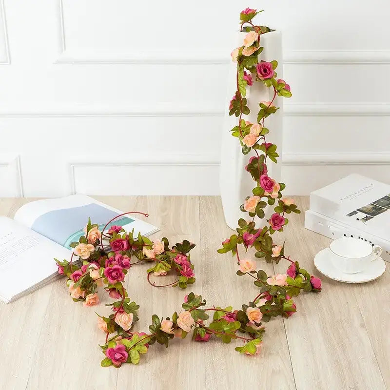 A delicate artificial rose vine garland with soft pink and peach blossoms intertwined with green leaves, designed for decorative use.
