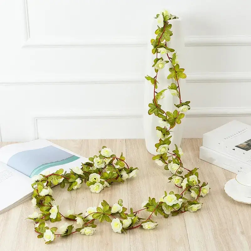A delicate white and green artificial flower vine with realistic petals and leaves, designed for decorative use.