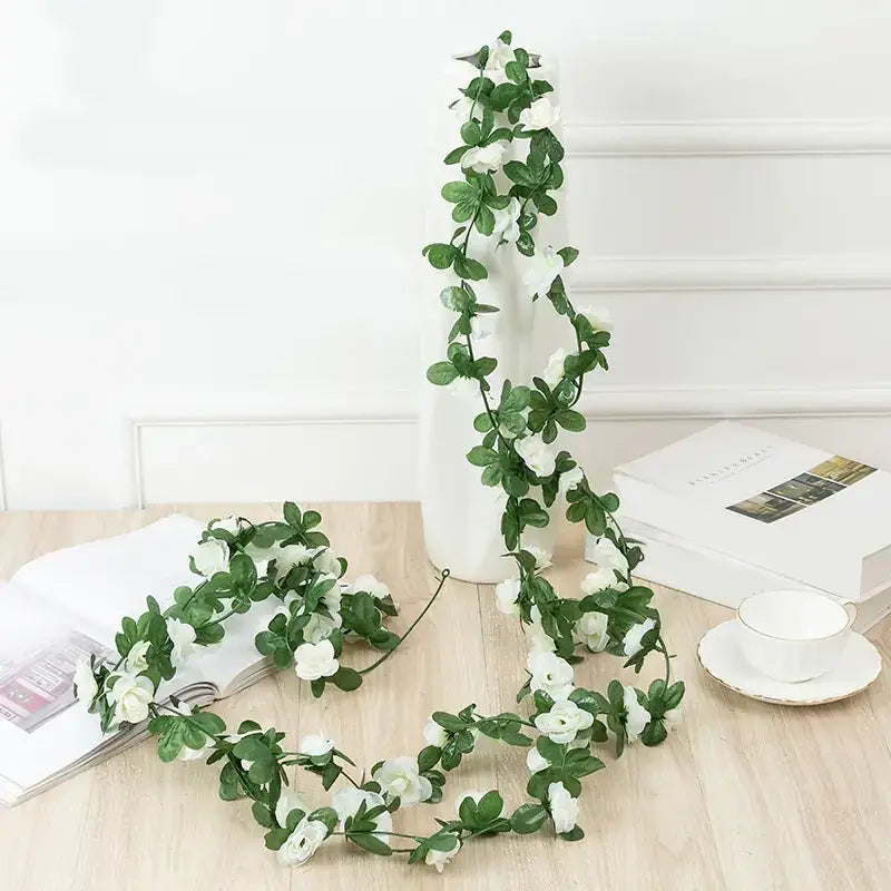 A delicate artificial floral garland with lush green leaves and clusters of white blossoms, crafted from synthetic materials to mimic the appearance of fresh vines.