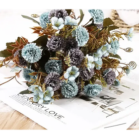 A delicate bouquet of artificial flowers in soft blue and gray hues, featuring layered petals and mixed greenery with subtle gold accents.
