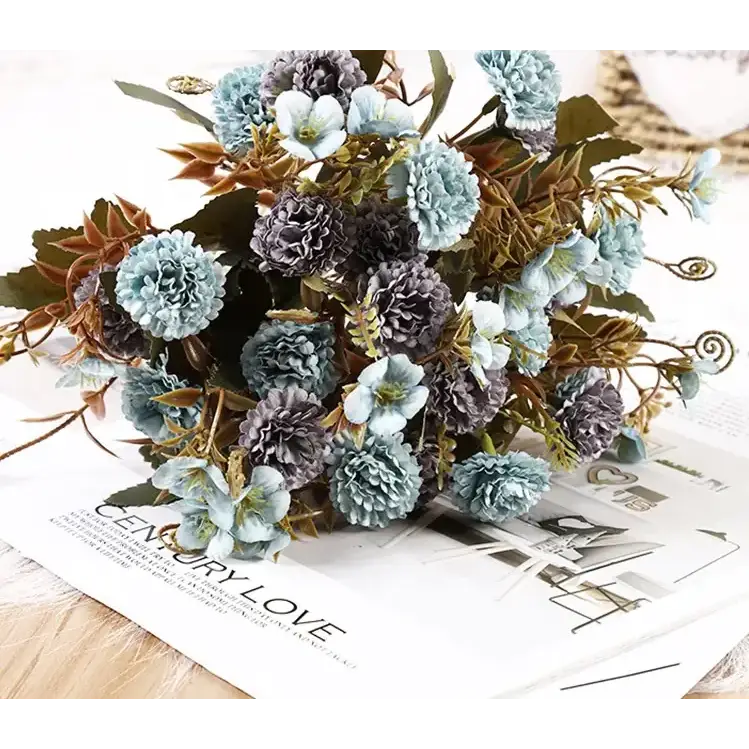 A delicate bouquet of artificial flowers in soft blue and gray hues, featuring layered petals and mixed greenery with subtle gold accents.