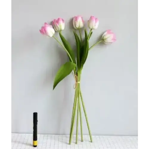 A bouquet of artificial pink and white tulips with green stems and leaves, tied together at the base.
