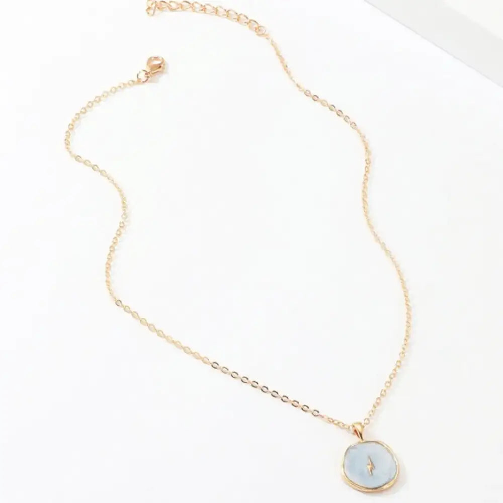 A delicate gold-toned chain necklace featuring a round, light blue pendant with a subtle lightning bolt design.