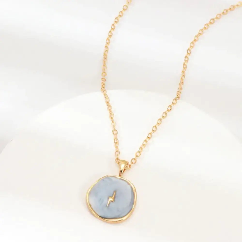 Gold-toned necklace with a round, light blue pendant featuring a small lightning bolt design.