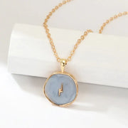 Gold-toned necklace with a round, light blue enamel pendant featuring a small gold lightning bolt design.