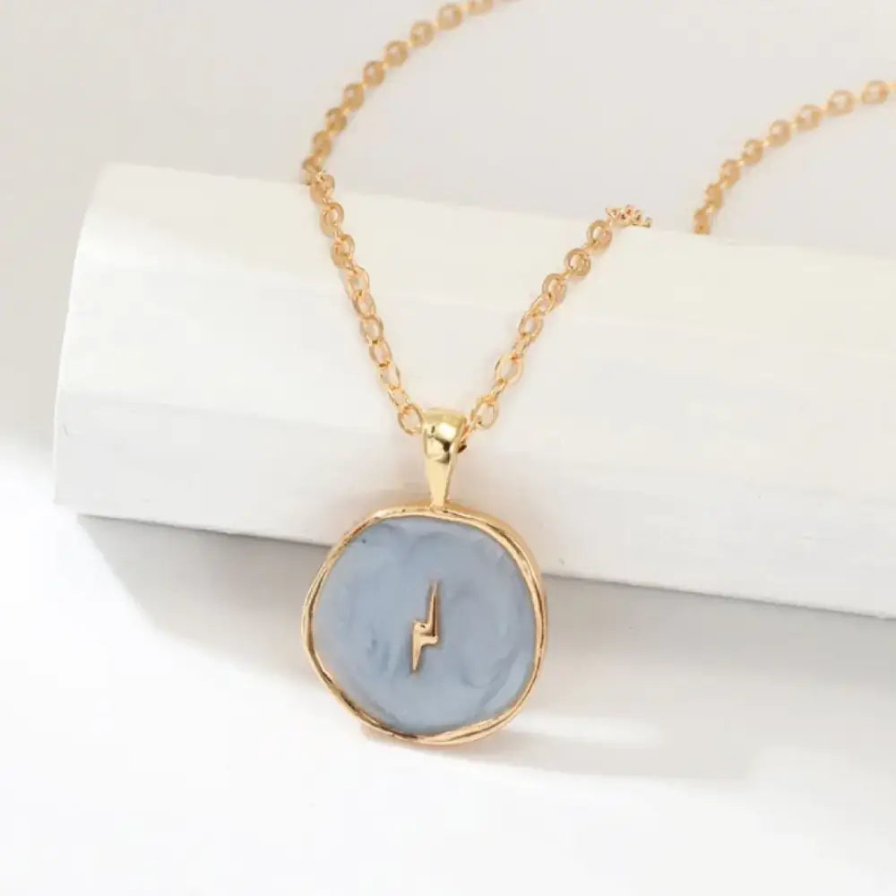 Gold-toned necklace with a round, light blue enamel pendant featuring a small gold lightning bolt design.