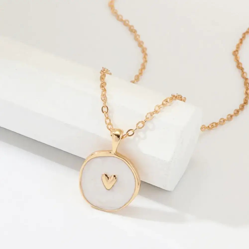 Gold-toned necklace with a circular pendant featuring a small heart charm set in white mother-of-pearl.