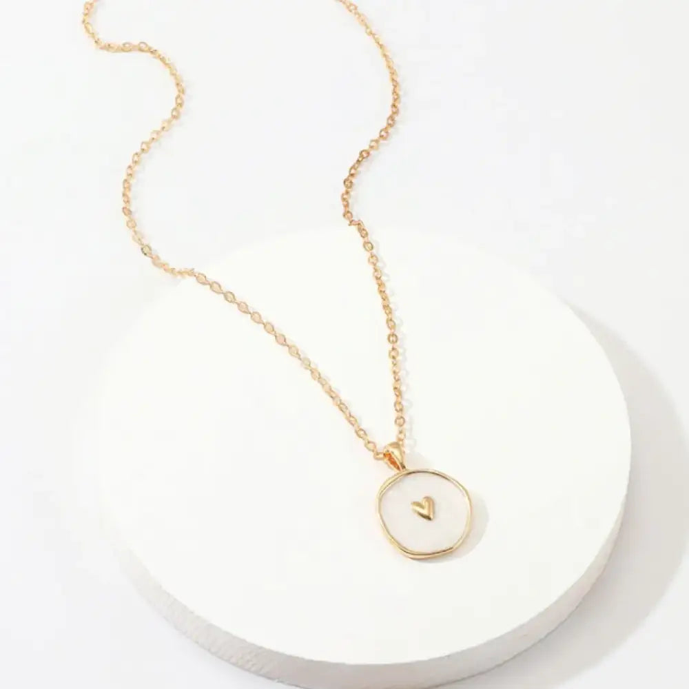 Gold-toned necklace with a delicate chain and a circular pendant featuring a small, embossed heart in the center.