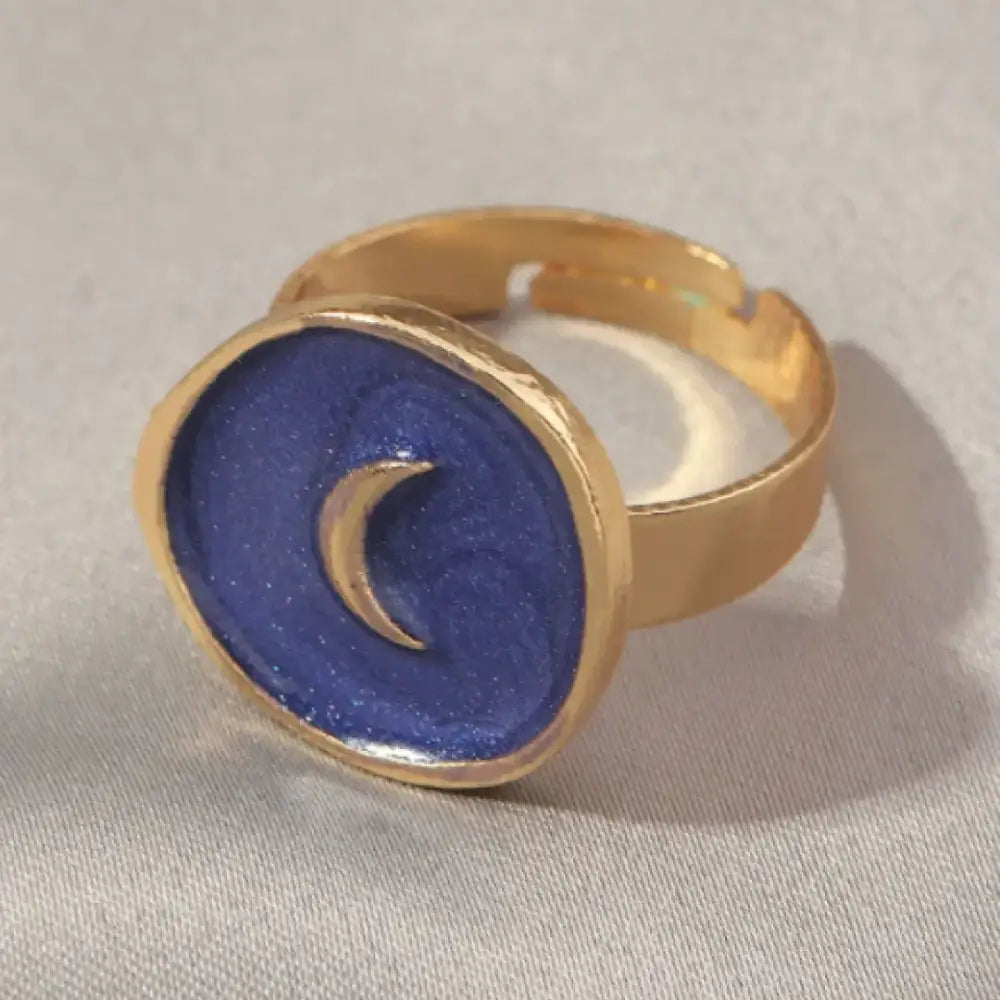 Gold-toned adjustable ring featuring a circular blue enamel face with a glittery texture and a raised crescent moon design.