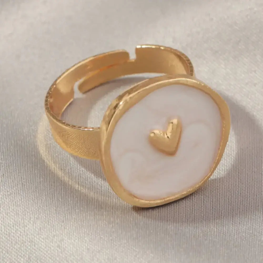 Gold-toned adjustable ring with a round, off-white enamel face featuring a small gold heart in the center.