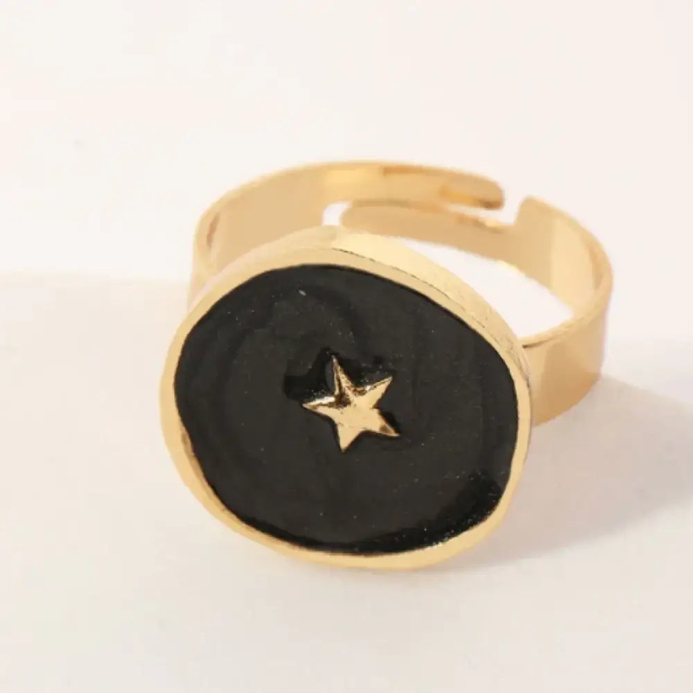 Gold-toned adjustable ring with a black, textured circular face featuring a small gold star in the center.